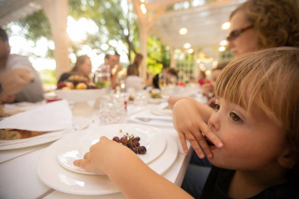 Curios lapsi syö viinirypäleitä pöydässä ulkopuolella ravintola
 - Valokuva, kuva