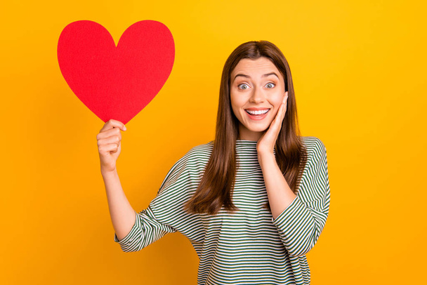Photo of gorgeous cool girl rejoicing about having been gifted big red heart for valentine day while isolated with yellow background - Foto, Imagen