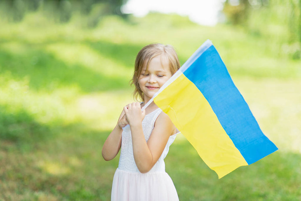 happy little girl with fluttering blue and yellow flag of Ukraine smiling and walking in field at sunny summer day, Ukraine Independence Day concept - Photo, Image