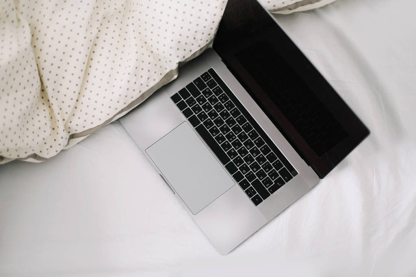 Laptop in bed on white linens. Work at home concept.  Flat lay, top view, lifestyle, minimalist workspace background.  - Фото, зображення