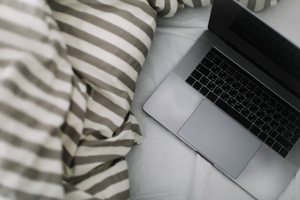 Laptop in bed on white linens. Work at home concept.  Flat lay, top view, lifestyle, minimalist workspace background.  - Photo, Image