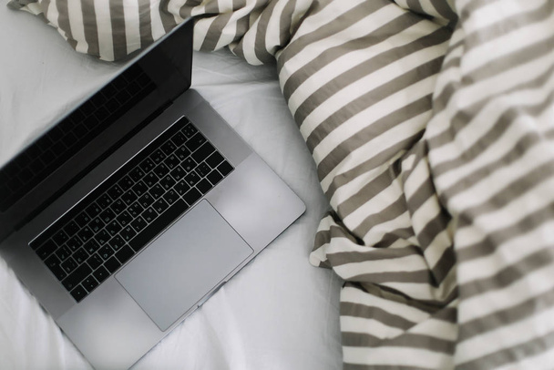 Laptop in bed on white linens. Work at home concept.  Flat lay, top view, lifestyle, minimalist workspace background.  - Fotó, kép