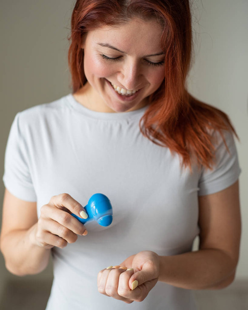 Red-haired girl dries nail polish with a pocket fan. An inventive woman makes herself a manicure in her own home. Small fan. Happy woman blowing on a bright manicure by the air flow. - Foto, Imagen