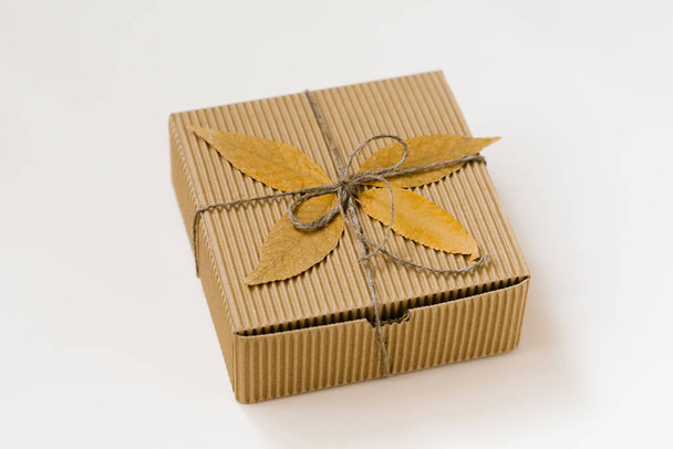 craft gift box, tied with string with a bow and autumn fallen leaves on a beige background. Autumn shopping discounts - Photo, Image