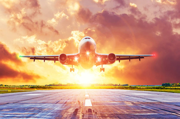 Flugzeug landet bei strahlendem Sonnenuntergang mit schönen Wolken auf Landebahn mit eingeschaltetem Landelicht. - Foto, Bild
