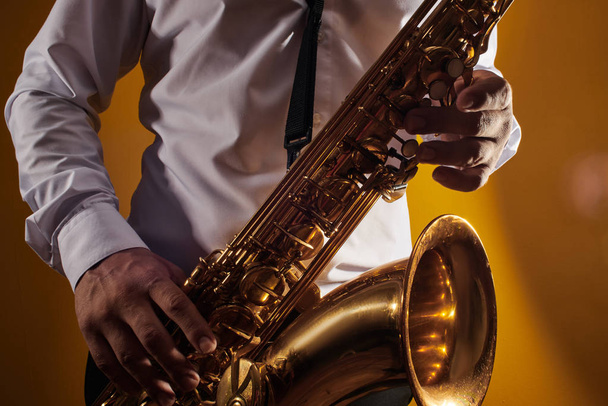 Portrait of professional musician saxophonist man in  white shirt plays jazz music on saxophone, yellow background in a photo studio, side view - Photo, image