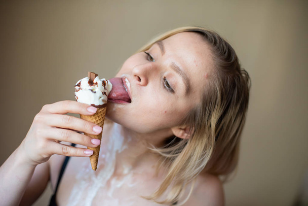 Sexy blonde licks a waffle cone. Ice cream is melting, erotically draining through the body of an attractive woman. Beautiful girl smeared with ice cream. - Zdjęcie, obraz