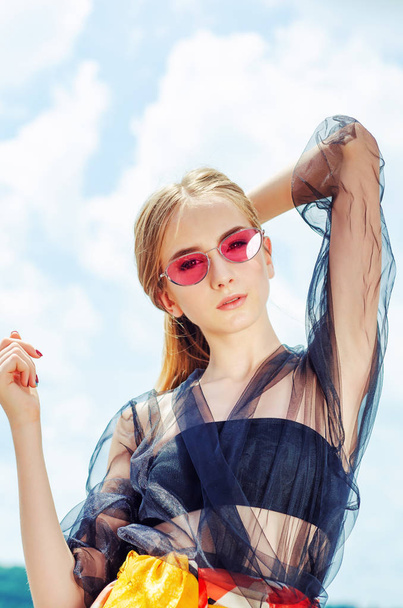 Young girl in red sunglasses posing over sky background - 写真・画像