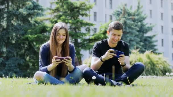 Happy friends play mobile game on smartphone, sitting on the grass in the park. - Footage, Video