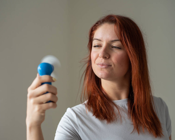 Portrait of a red-haired woman with a pocket fan in her hands. A girl refreshing in the heat of the wind blowing away from a wireless electric device. Enjoy the cool airflow from the air conditioner. - Foto, Imagem