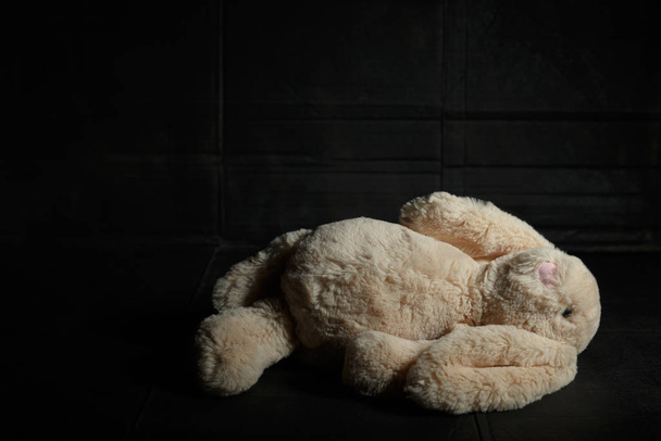 Soft toy rabbit on a dirty dark background in the beam of hard light with shadow. Lost childhood concept - Zdjęcie, obraz
