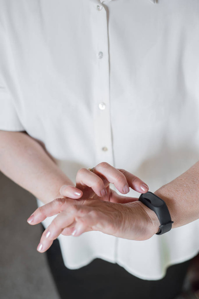 An elderly woman in a white blouse is wearing a fitness bracelet. Smart watch on the hand of an old woman. Pensioner Using Fitness Tracker. - Foto, Imagem