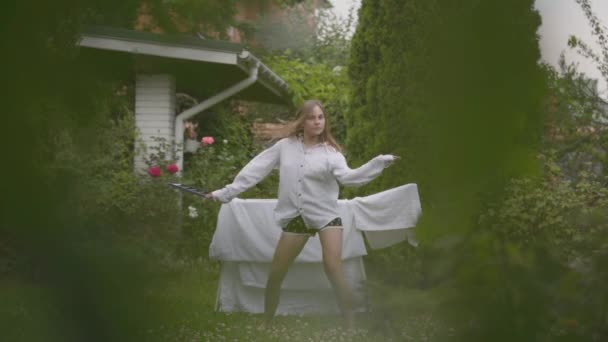 Viehättävä valkoihoinen nuori nainen hauskaa laulaa ja tanssia takapihalla, kun teet talon työtä pellavan kanssa. Pesupäivä, pesupäivä. Hidastus
. - Materiaali, video