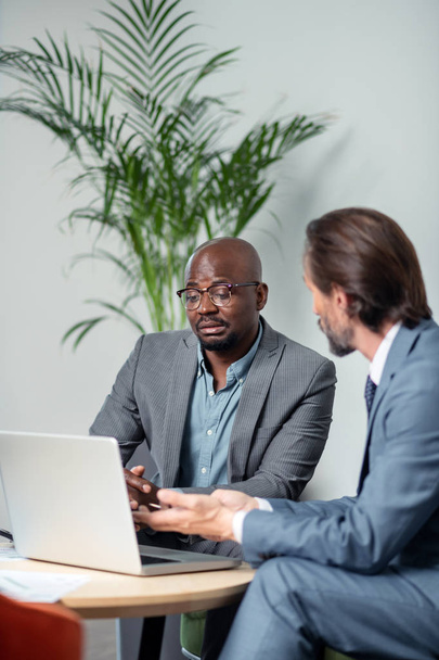 Dark-skinned employee sitting near laptop and talking to boss - Foto, afbeelding