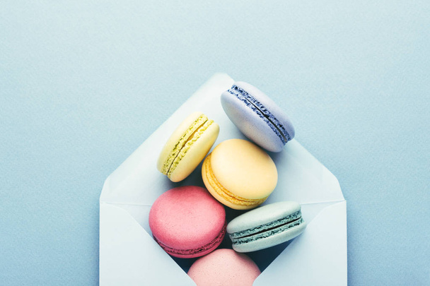 Colorful macarons in envelope on blue background. - Фото, изображение