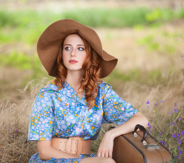 Redhead girl with suitcase sitting at autumn grass - Фото, зображення