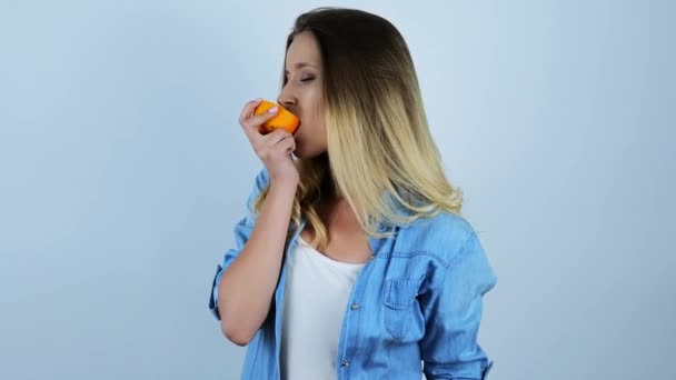 fiatal gyönyörű szőke nő harapós fele friss narancs az elszigetelt fehér háttér - Felvétel, videó