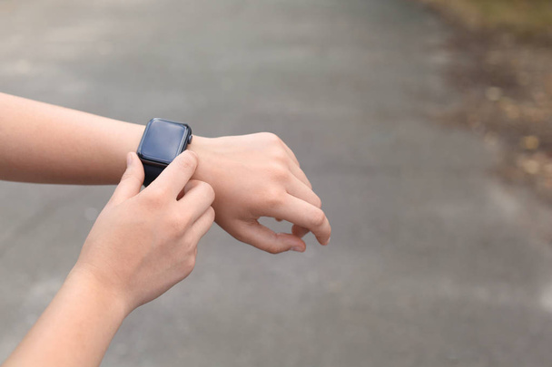 Young woman checking pulse with smartwatch on street, closeup. Space for text - 写真・画像