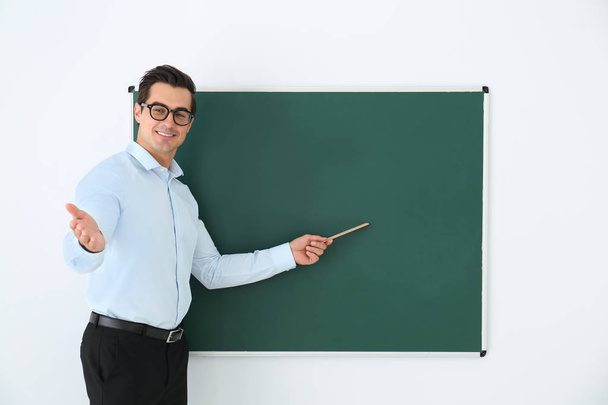 Young teacher with ruler near blank chalkboard in classroom. Space for text - Foto, afbeelding
