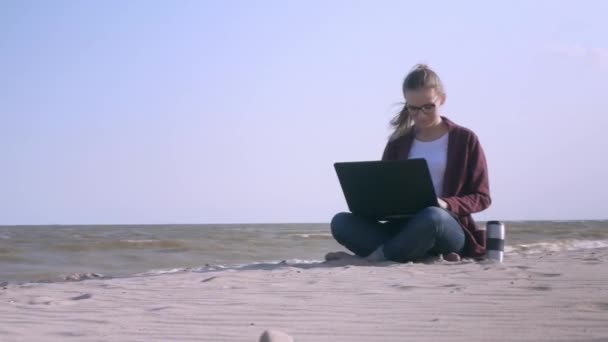 A fiatal, jóképű nő dolgozik egy laptop a strandon a beállítás nap. Fiatal üzletember dolgozik a tengerparton naplementekor. Szabadúszóként működik a tengerparton. - Felvétel, videó