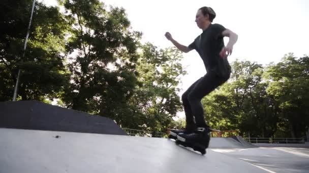 Man inline roller blader performing jumps at local skate park, Young gut on roller skates perform tricks on the ramp, freeze on the top then turn back and slide down. Extreme sports outdoors. Low - Footage, Video
