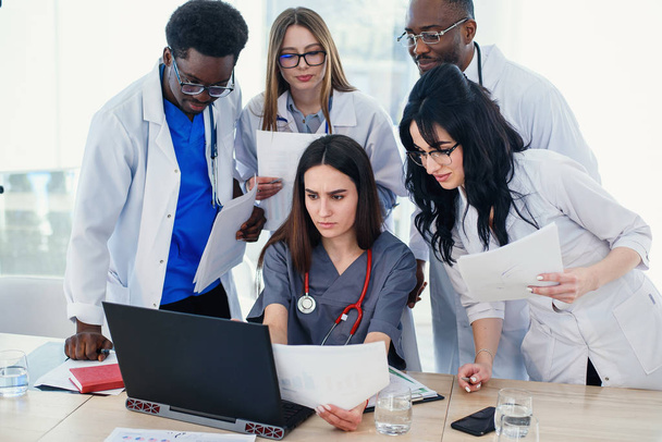 Gruppe junger multinationaler Ärzte während der Arbeit mit Laptop im Konferenzraum. - Foto, Bild