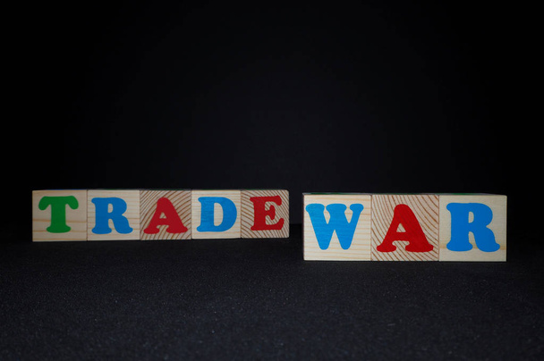 テキストと木製のアルファベットのおもちゃのブロック:貿易戦争。コピースペースを持つ黒い背景に孤立した子供の多色Abcキューブ。アメリカと中国の貿易戦争概念. - 写真・画像