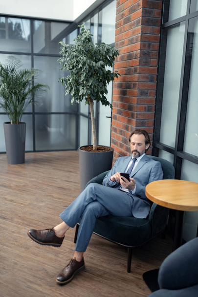 Bearded businessman using his phone while waiting for colleague - Photo, image