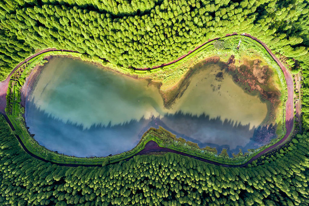 Silmälasien muotoinen drone maisema. Ylhäältä alas antenni näkymä pieni lampi keskellä metsää, heijastaa pilviä taivaalla. Lintunäkymä Empadadas laguunille Azoreilla, Portugali
.  - Valokuva, kuva