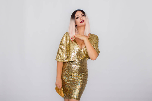 Charming young blonde haired woman wearing elegant gold evening dress and holding gold color clutch in her hands - Fotoğraf, Görsel