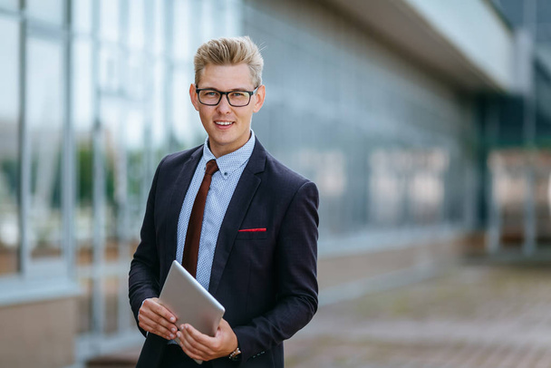 Happy smiling businessman with digital tablet. Portrait of a Male executive manager in trendy clothes with tablet PC in hand on background of office building. Modern technology concept - Foto, Bild