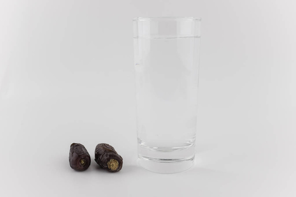 glass of water and dried dates on white background - 写真・画像