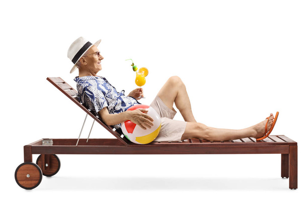 Elderly man lying on a sunbed drinking a cocktail and holding an - Fotoğraf, Görsel