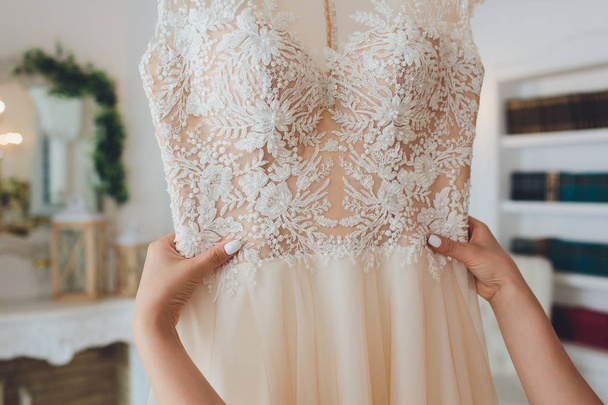 Robe de mariée rose riche accrochée à un lustre dans une chambre blanche
. - Photo, image