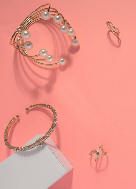 Vista superior de pulseras y anillos dorados sobre fondo rosa
 - Foto, imagen