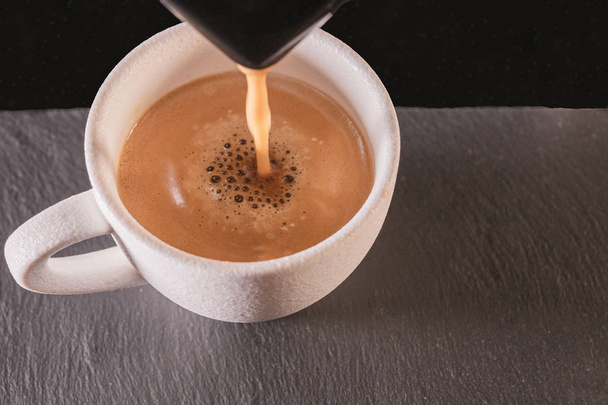 Κοντινό κομμάτι ενός μηχανήματος που ρίχνει καφέ πάνω από ένα λευκό φλιτζάνι - Φωτογραφία, εικόνα
