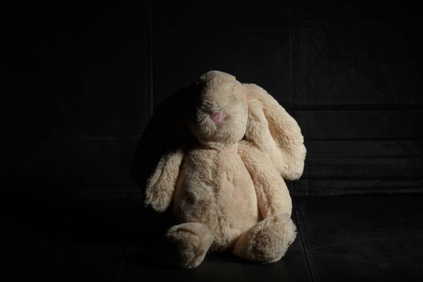 Soft toy bunny on a dirty dark background in the beam of hard light with shadow. Lost childhood concept - Valokuva, kuva