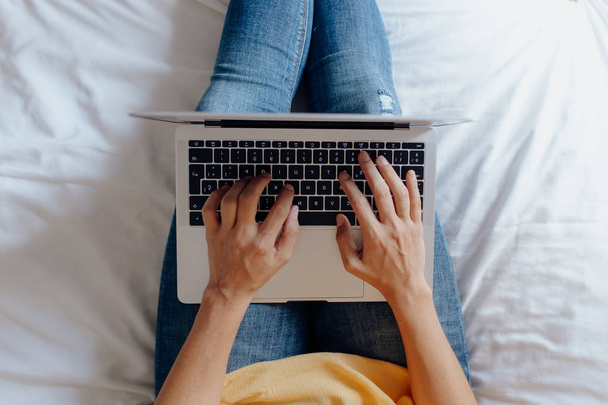 Unrecognizable woman sitting on the bed typing on the laptop - Foto, Bild