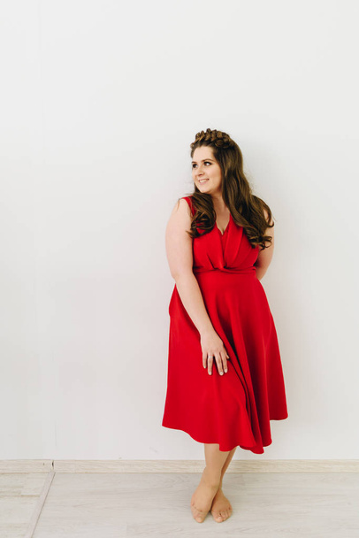 Una hermosa mujer caucásica con un vestido rojo de moda y de pie en el fondo blanco
 - Foto, Imagen