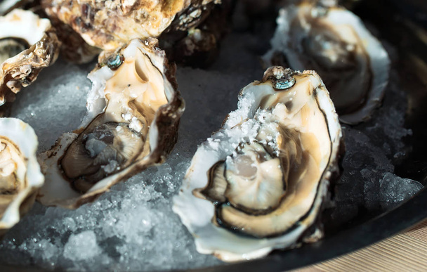 Oysters on a black plate on a wooden background. - Fotó, kép