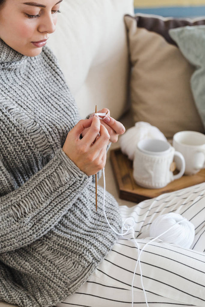 girl in a warm gray sweater knits sitting on a sofa in a cozy interior hygge - Zdjęcie, obraz