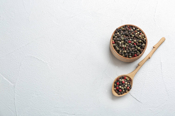 Bowl and spoon with different peppercorns on light table, top view. Space for text - Foto, Imagen