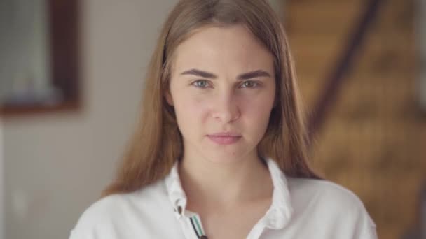Portrait of confident carefree cute woman with different colored eyes looking at camera indoors. Young girl with a headache rubs her head with her hands. Migraine, sick headache. Real people series. - Séquence, vidéo