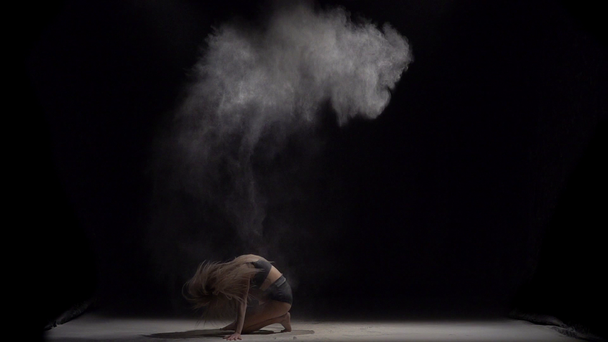 Dziewczyna rzuca cząstki pyłu w powietrzu na czarnym tle. Zwolnionym - Materiał filmowy, wideo