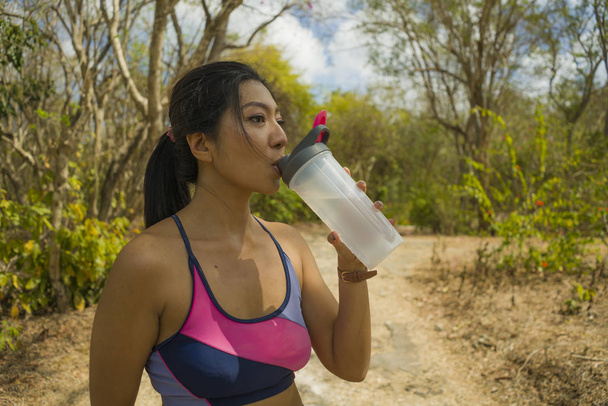 Outdoors lifestyle portrait of young attractive tired and thirsty Asian woman drinking water after hard running workout cooling off at beautiful green park
  - Фото, изображение