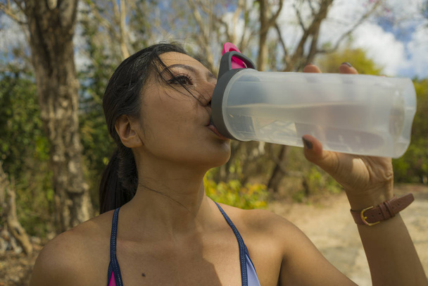 outdoors lifestyle portrait of young attractive tired and thirsty Asian woman drinking water after hard running workout cooling off at beautiful green park  - Foto, imagen