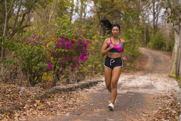 young attractive and exotic Asian Indonesian runner woman in jogging workout outdoors at countryside road track nature running sweaty pushing hard - 写真・画像