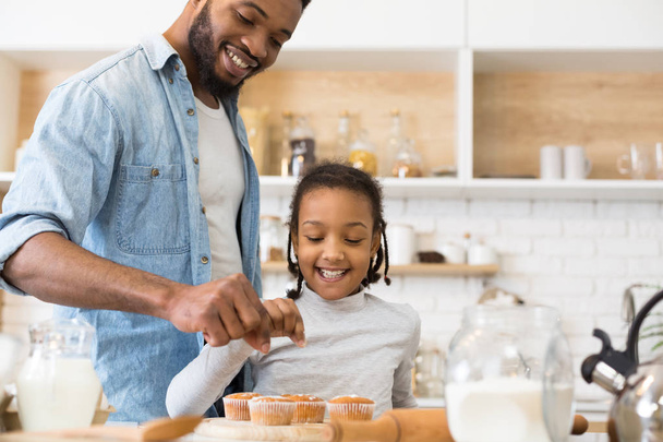 Menina afro feliz e seu pai decorando muffins
 - Foto, Imagem