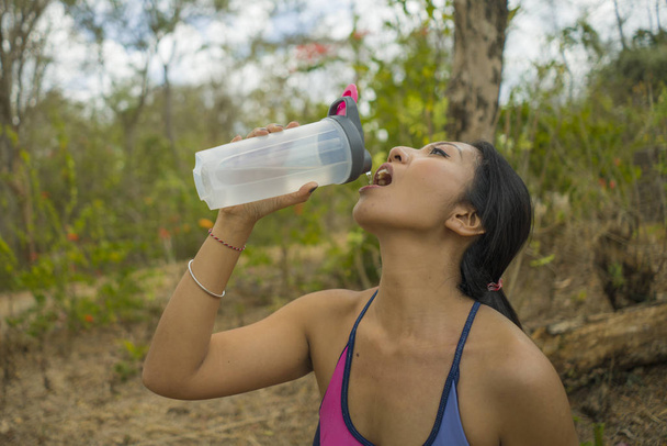 outdoors lifestyle portrait of young attractive tired and thirsty Asian woman drinking water after hard running workout cooling off at beautiful green park  - Photo, Image