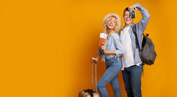 Young couple posing with tickets and camera over yellow background - Photo, Image